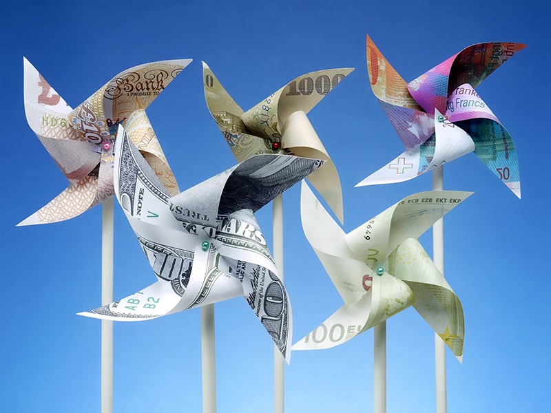 Toy windmills cut from five major world currency banknotes over blue sky