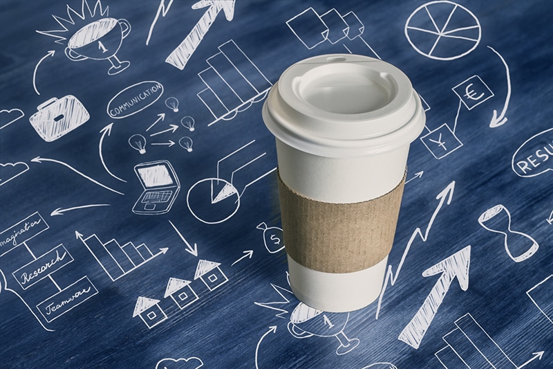 Coffee cup on wooden desktop with business drawings