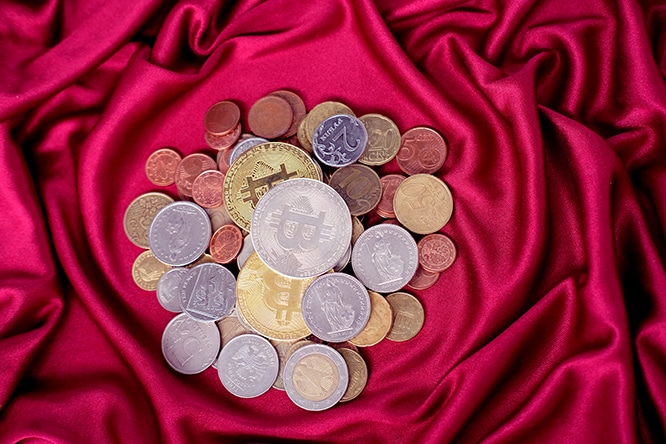 slide of metal coins, currencies of different countries close-up, bitcoins on a red luxury drapery
