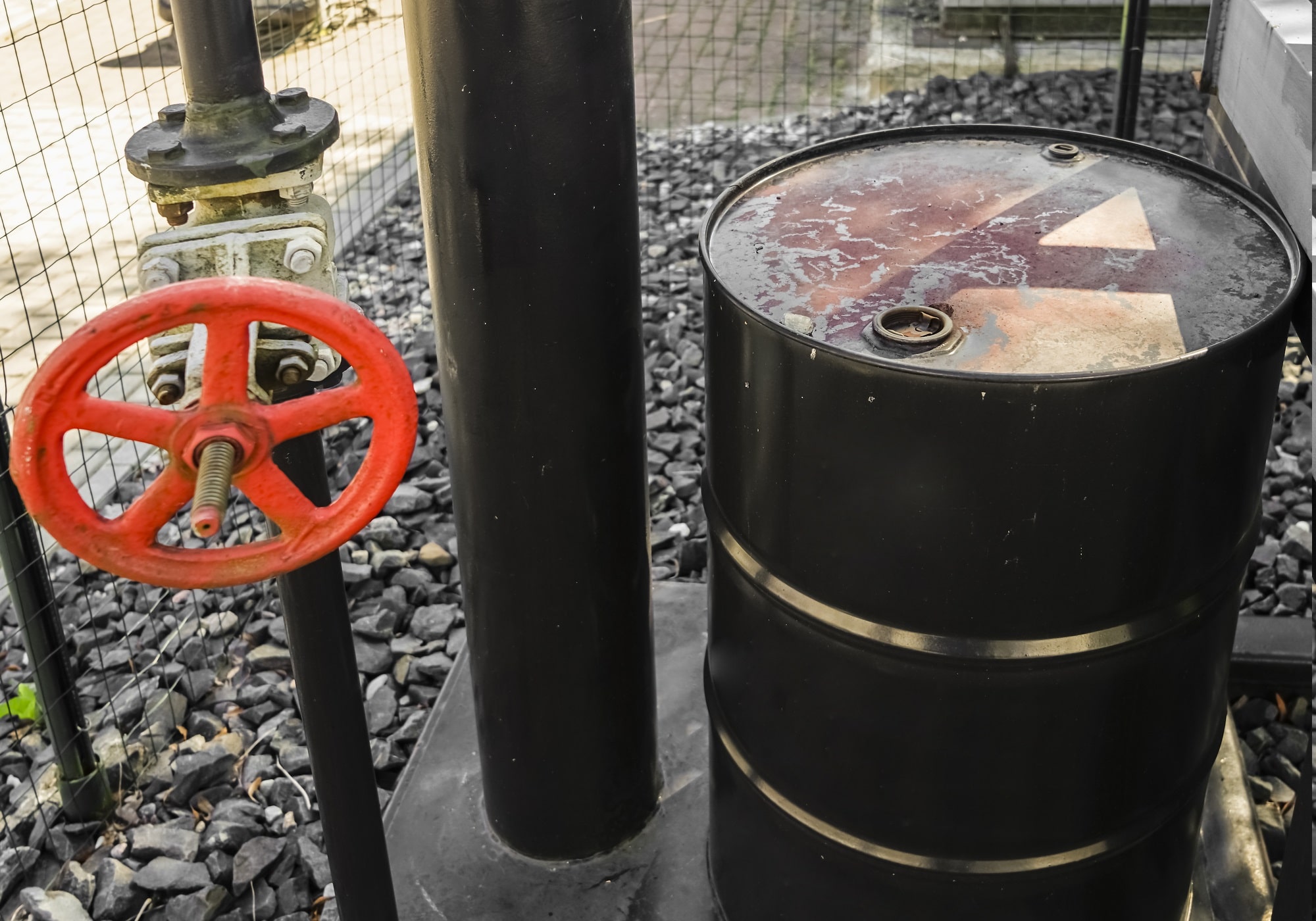 Black pipe and red valve near oil barrel.