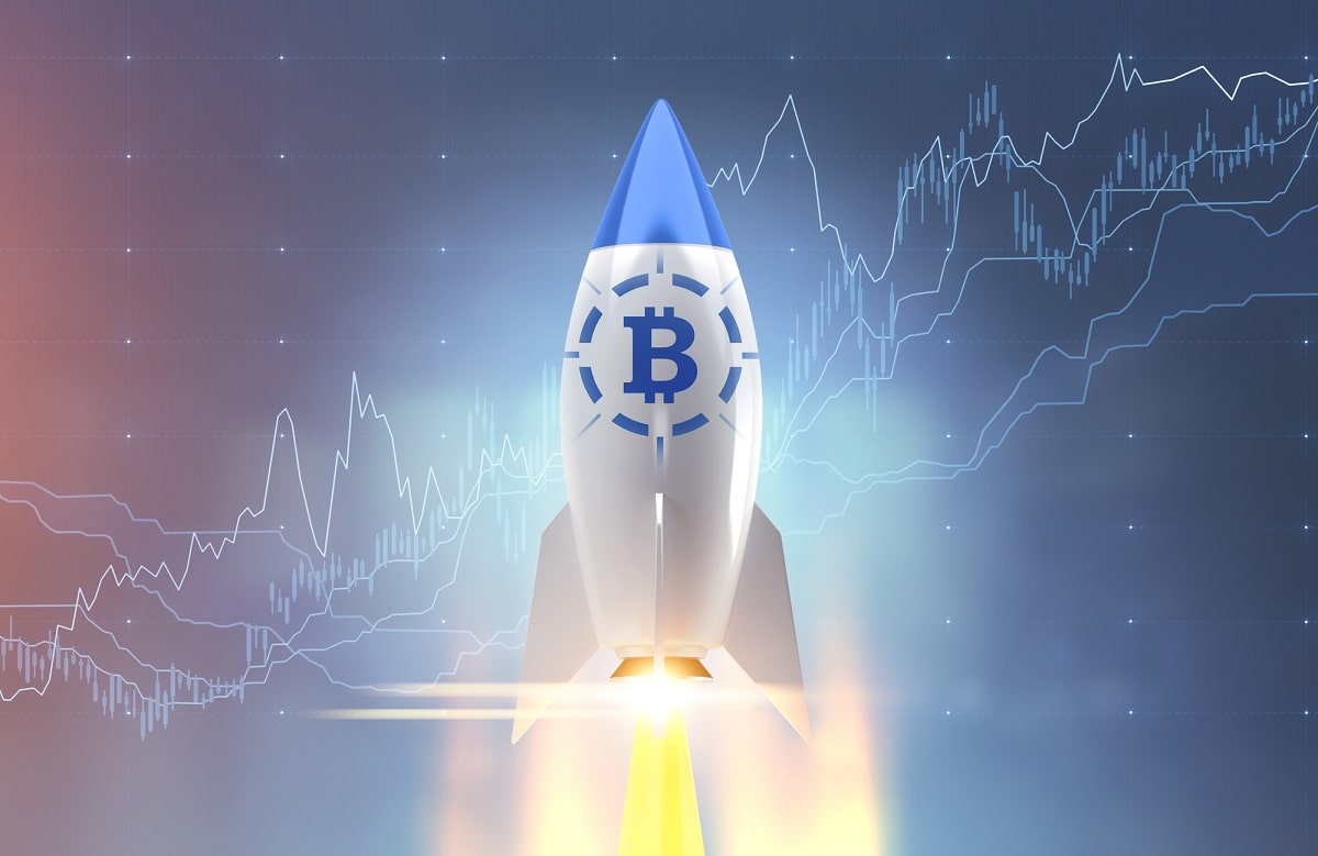 White and blue rocket with a bitcoin symbol starting up. A blurred blue background with graphs.