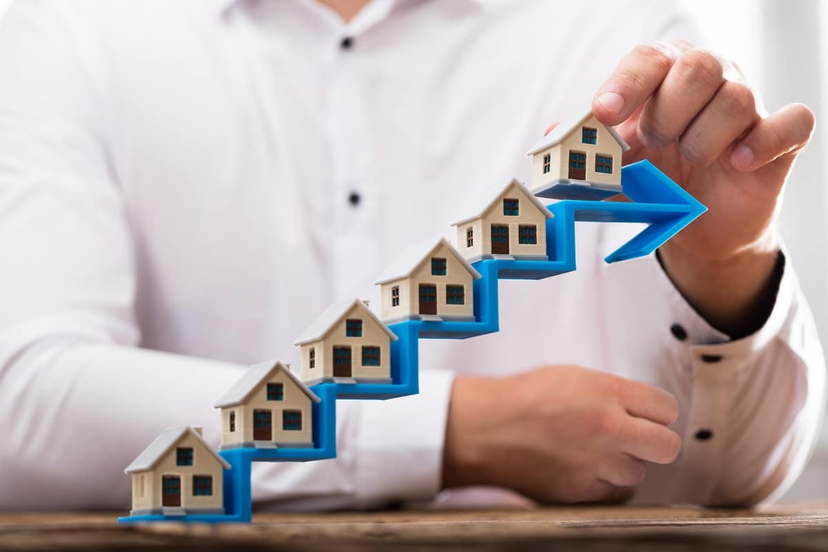 Close-up of a businessman's hand placing house models on increasing blue arrow staircase