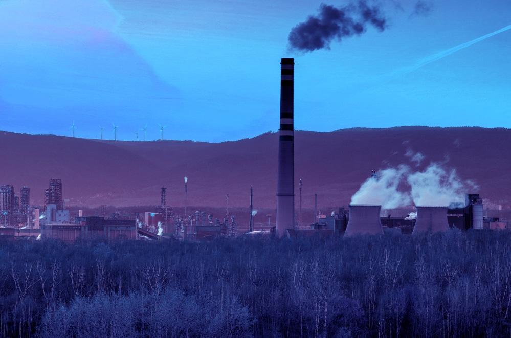 Heavy industry, petrochemical factory with wind power turbines on the hill.