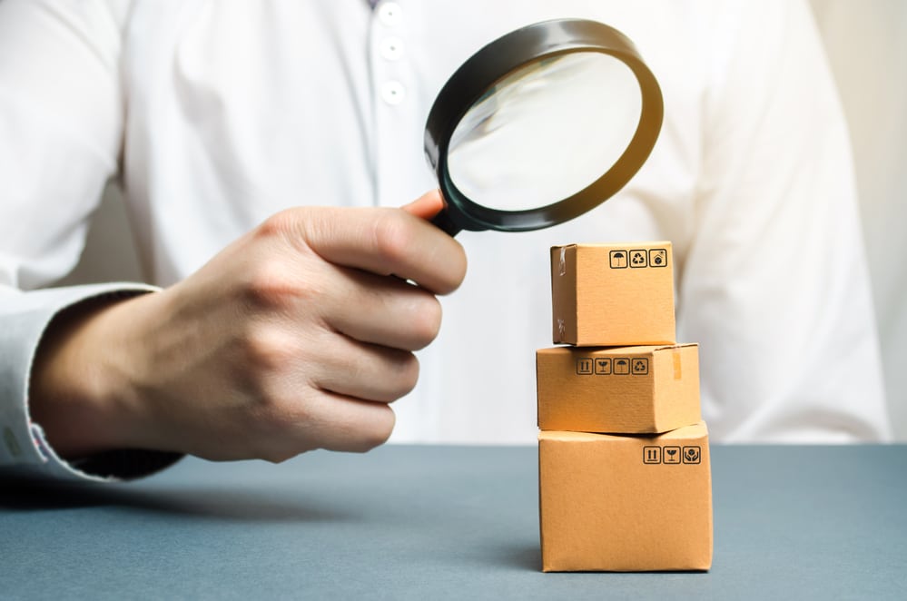 A man holds a magnifying glass above the boxes. Examination of goods for the presence of contraband, prohibited goods, defects. Quality control, authentication. study of consumer sentiment