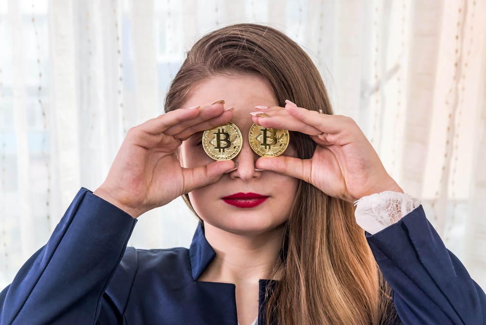 Pretty young woman holding bitcoins before her eyes