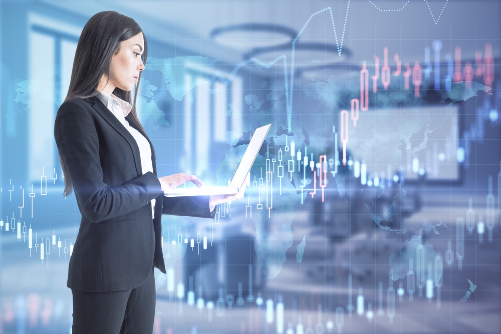 Pretty young european businesswoman with laptop standing in blurry office interior with forex chart. Trade and stock market concept. Double exposure