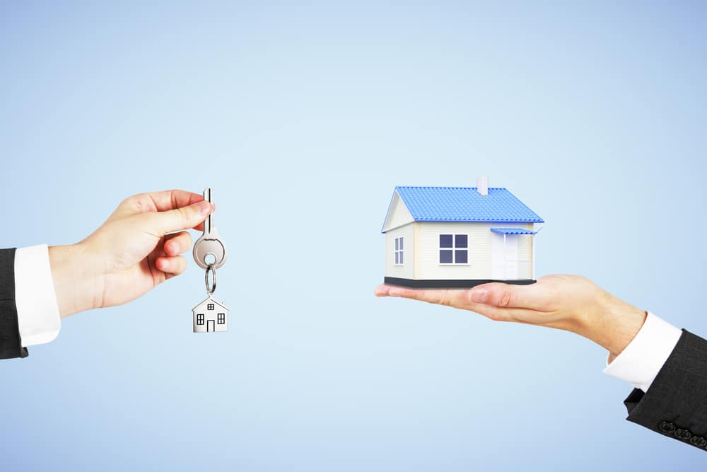 Real estate concept with man hand with key and house in another hand